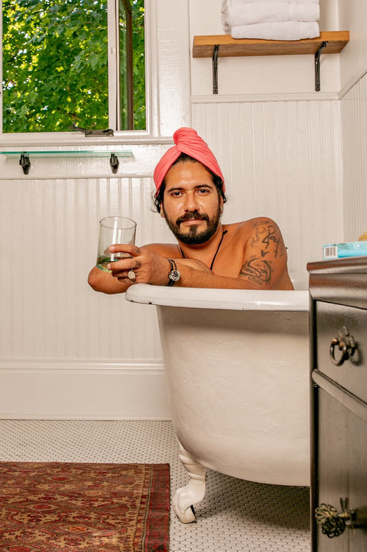 man dries his hair with a Capillum Bamboo Hair Towel in Pink while taking a bath