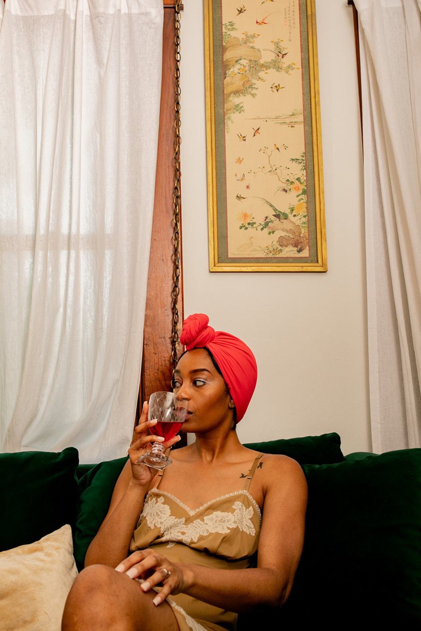woman sips on cocktail while drying her hair with Capillum bamboo hair towel in red.