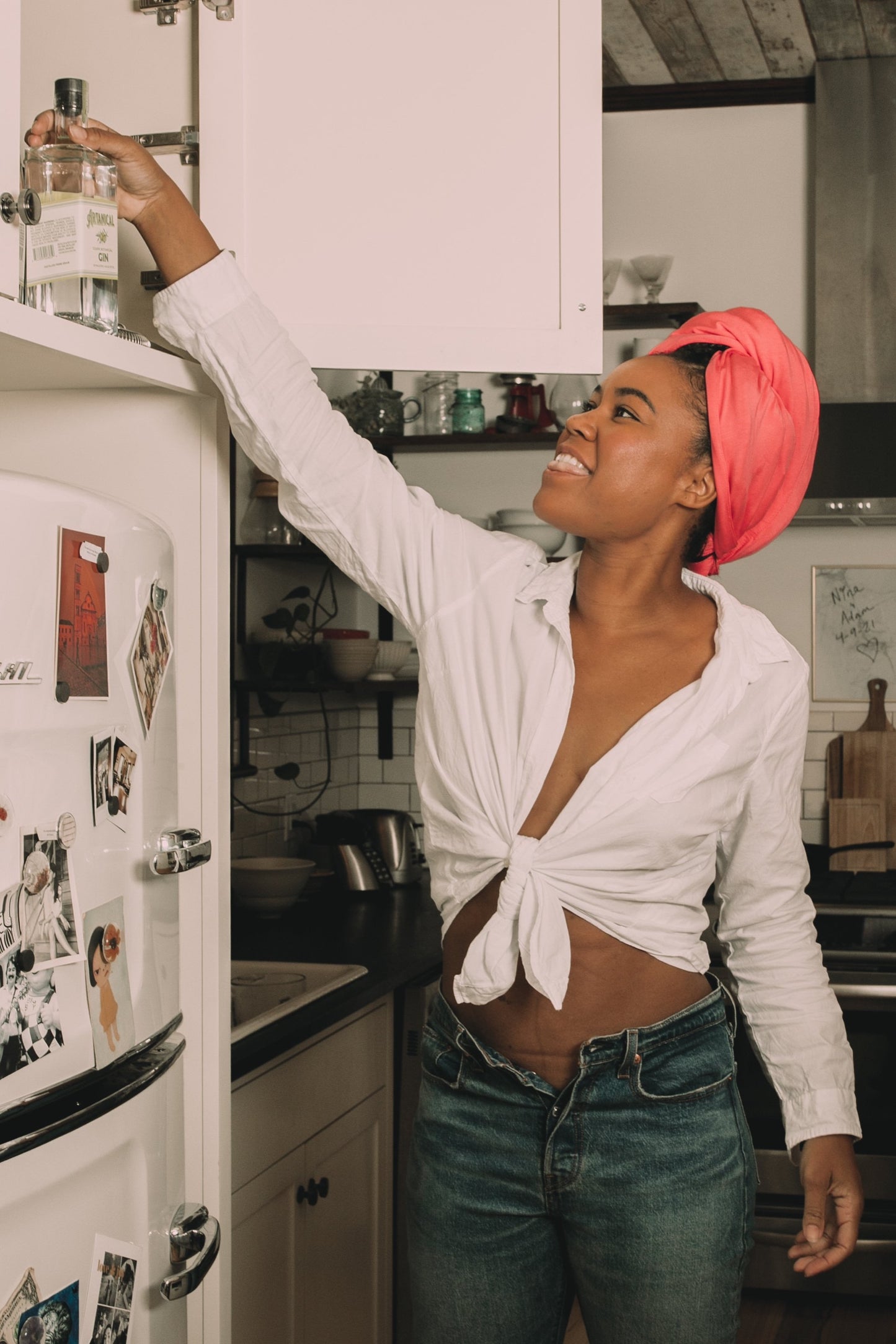 woman grabs a bottle from a cabinet while wearing her Capillum Bamboo hair towel in pink to rapidly dry her hair.