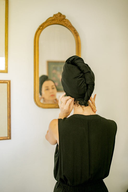 woman gets ready in the mirror while rapidly drying her hair with a Capillum bamboo hair towel in black