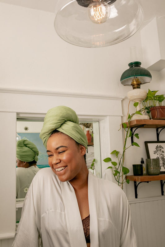 woman smiles in bathroom while drying her hair with the Capillum Bamboo hair towel in green 