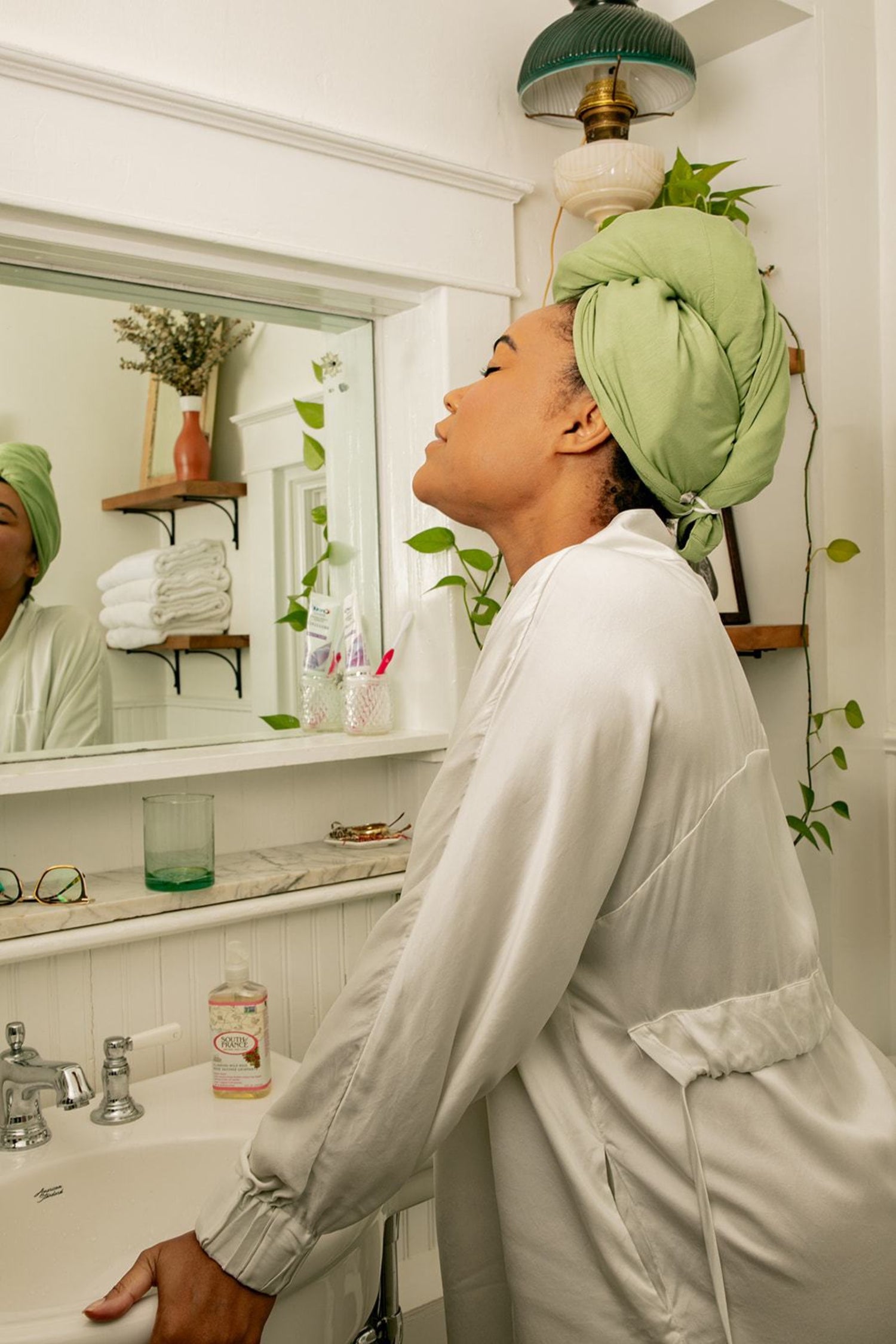 Woman looks into mirror wearing a Capillum hair towel imn green 