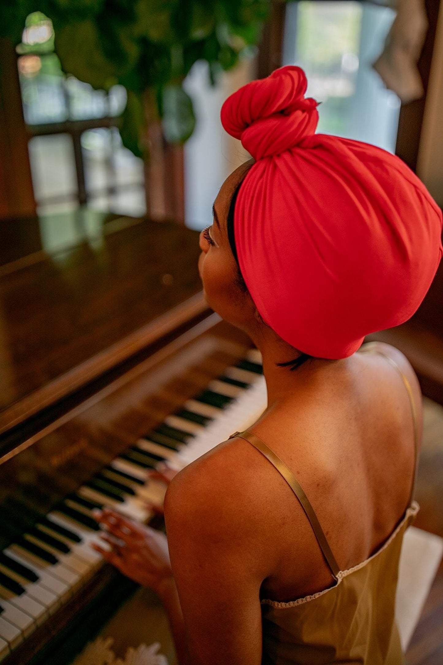 woman plays piano while she quickly dries her hair with her red bamboo hair towel by Capillum. 